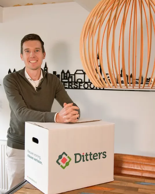 Een medewerker van Ditters Makelaars Amersfoort ondersteunt klanten bij de verkoop van hun woning en de voorbereidingen op hun volgende woonsituatie, weergegeven met een Ditters-verhuisdoos.