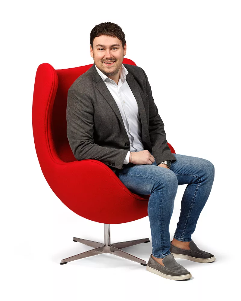 Thom van Ditters, verzekeringsadviseur, lachend portret in rode stoel.
