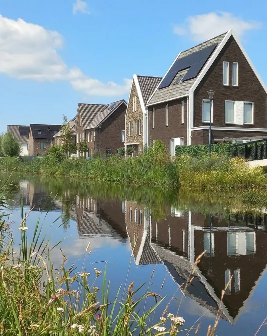 Moderne woningen in de buurt Veenendaal-Oost met uitzicht op het water, groene oevers en een brug in een rustige, nieuwbouwwijk.