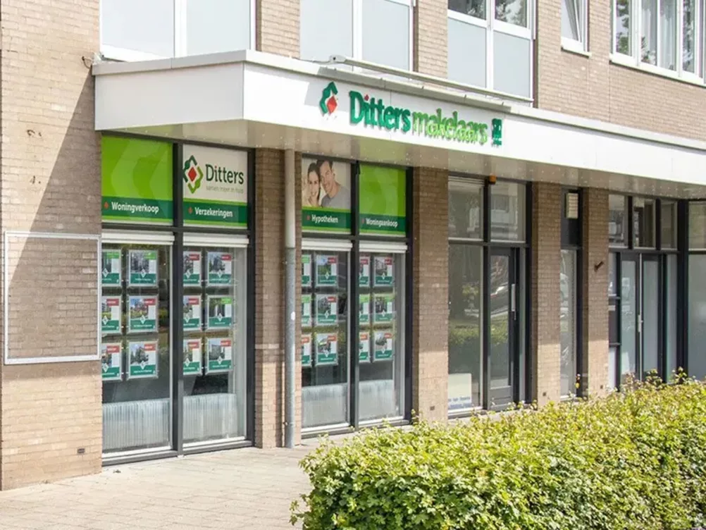 Buitenaanzicht van het kantoor van Ditters Makelaars Wageningen met etalagepresentaties van woningen en zicht op de diensten zoals woningverkoop, hypotheken en verzekeringen.