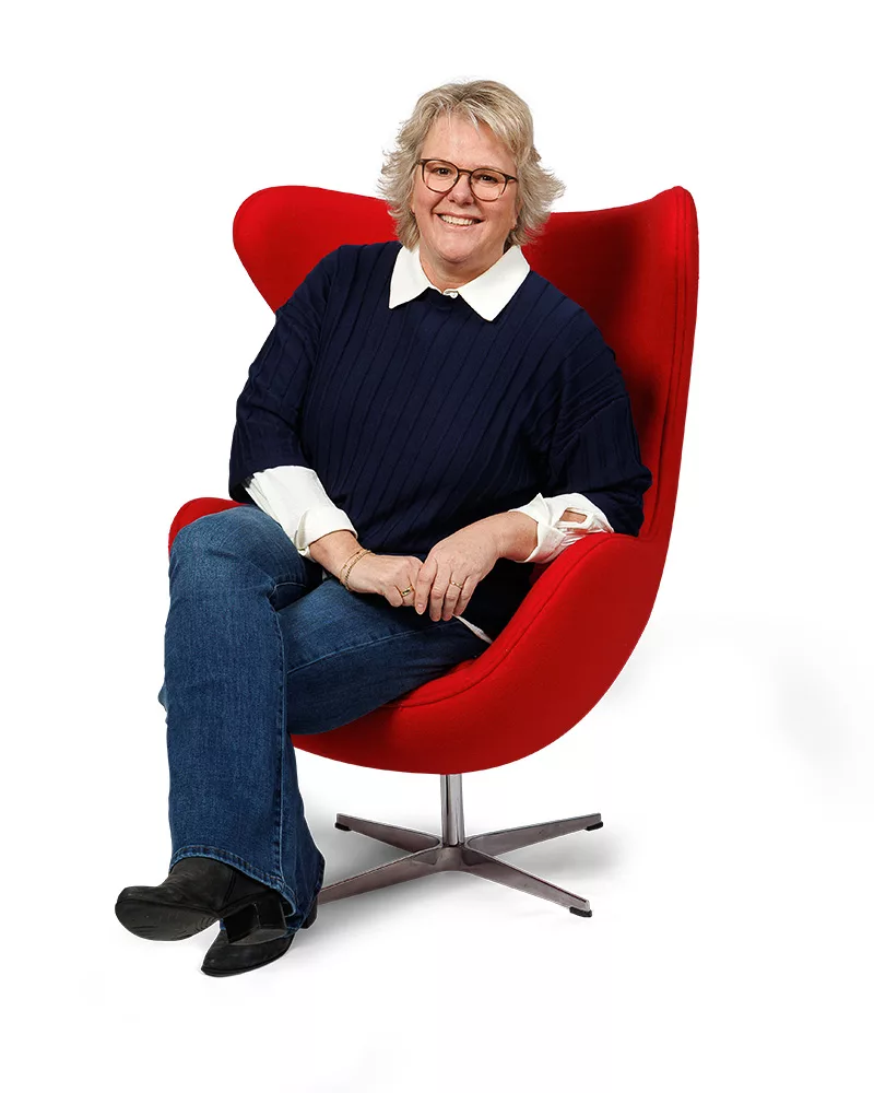 Diana van Ditters, binnendienst hypotheken, zittend in rode stoel, vriendelijk portret.